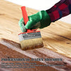 A hand holds a red handle of a professional paint brush with a green grip, applying paint to a wooden surface.