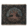 A dark woven throw blanket featuring a large tree silhouette and intricate foliage patterns in muted teal and rose tones.