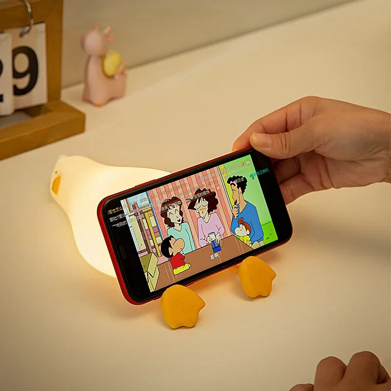 A hand holds a smartphone displaying a cartoon, with silicone duck shapes nearby.