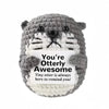 A gray crochet animal doll resembling a bear with a white face and a card that reads You're Otterly Awesome