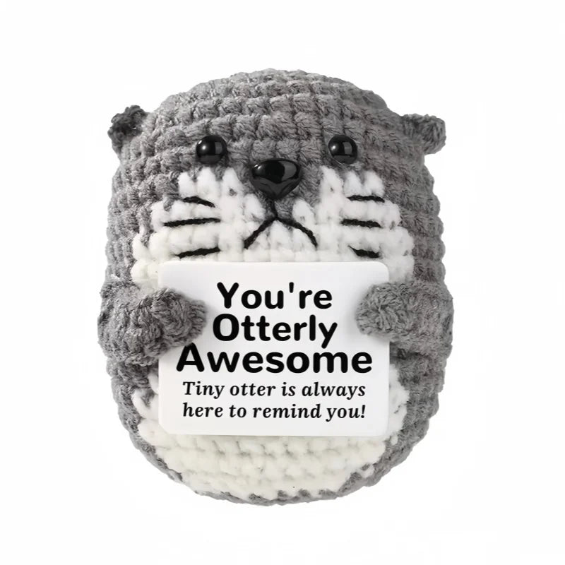 A gray crochet animal doll resembling a bear with a white face and a card that reads You're Otterly Awesome