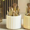 A white cylindrical organizer holding various gold and beige makeup brushes.