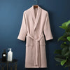 A light pink waffle knit robe hanging on a dark blue wall next to a green plant.