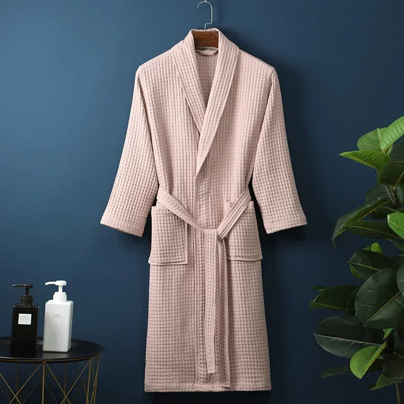 A light pink waffle knit robe hanging on a dark blue wall next to a green plant.
