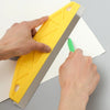 A hand is holding a yellow precision paint edger with an ergonomic handle and using a green tool to apply paint on white pape