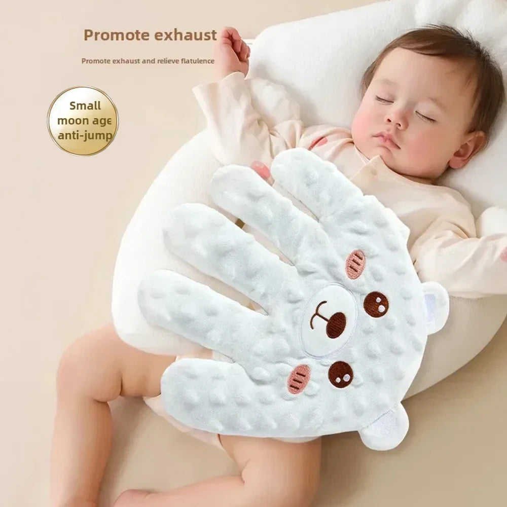 A white palm-shaped baby sleep pillow with a cute face design is shown next to a sleeping baby.