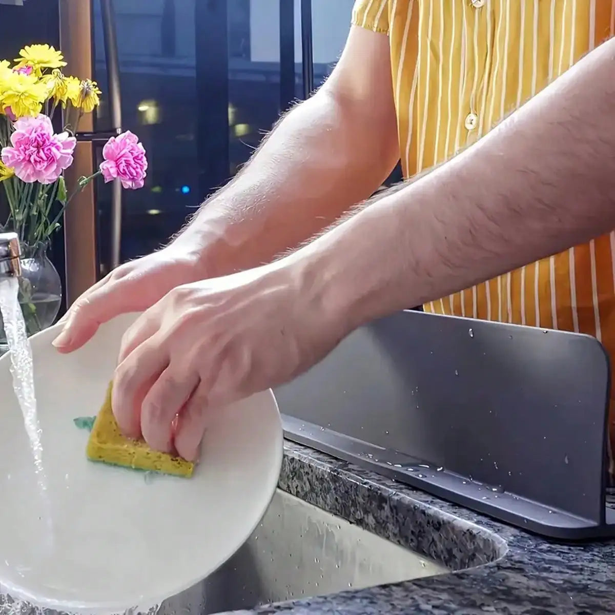 Eine Hand benutzt eine Silikon-Spülschutzhaube mit Saugnapf, um den Wasserfluss in einer Küchenspüle zu steuern.