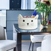 A white woven cotton rope storage basket with cat ears and a blue bow is displayed on a dark table.