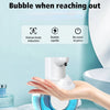 A hand is dispensing foam soap from a blue wall-mounted infrared automatic dispenser onto a toilet bowl.