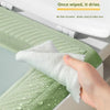 A hand is wiping a white, textured cleaning cloth on a light green toilet seat cover.