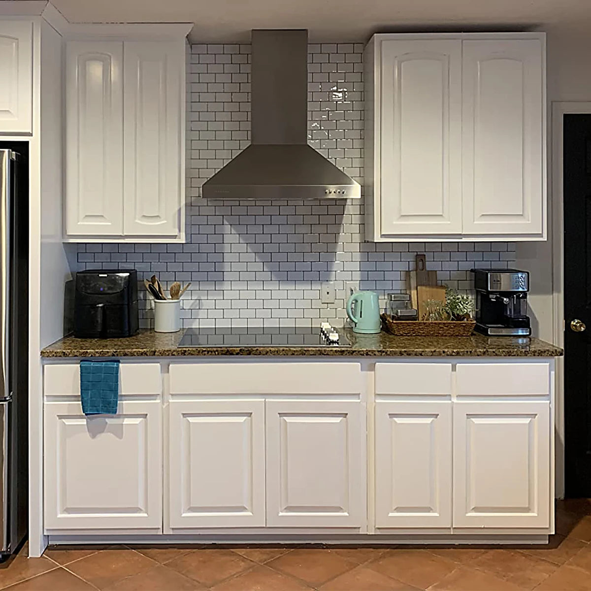 White kitchen cabinets with a speckled countertop and a stainless steel hood above them.