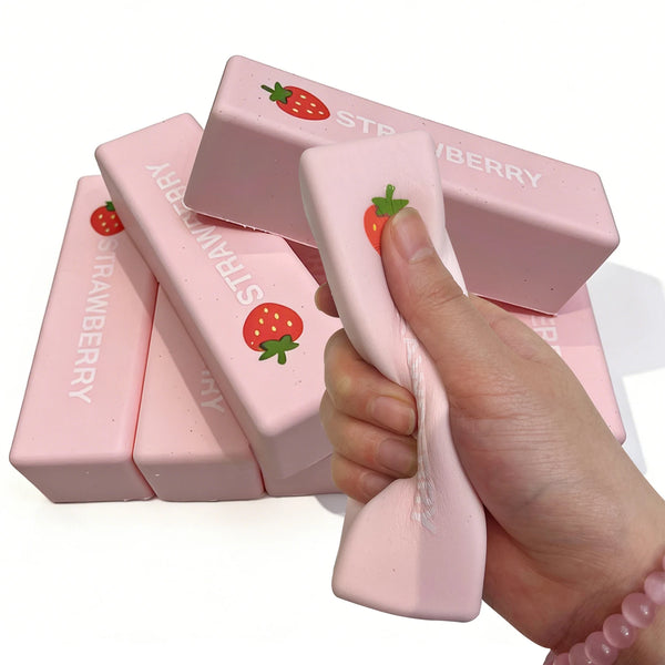 Une main serre un jouet anti-stress rose en forme de bloc de beurre de fraise.
