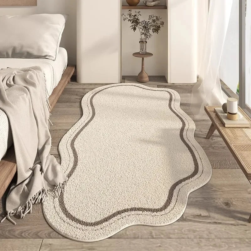 A beige irregular area rug with a subtle textured border placed on a light wood floor.