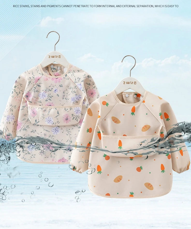 A light pink children's waterproof long sleeve feeding bib with a catch pocket, featuring floral and fruit patterns.