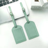 A pair of mint green PU leather luggage tags are displayed next to a silver laptop.