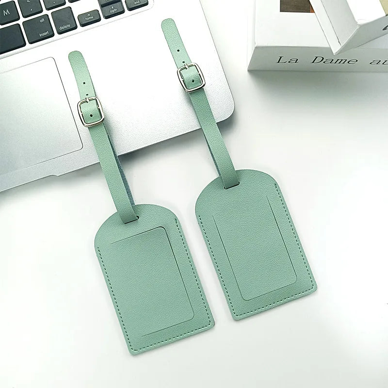 A pair of mint green PU leather luggage tags are displayed next to a silver laptop.