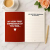 A red journal with lined pages and a title page for a love book is displayed on a marble surface.