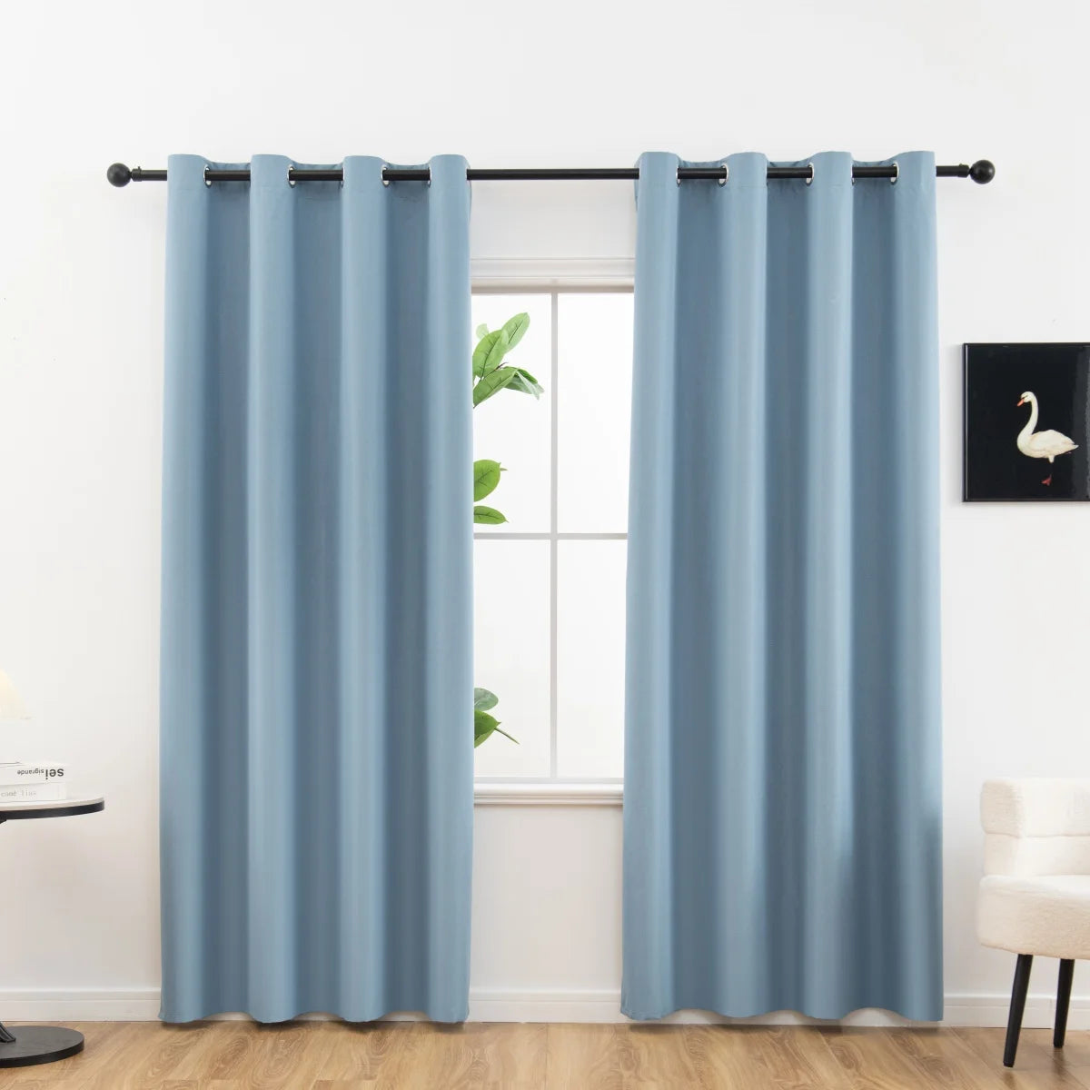 A pair of light blue blackout curtains hanging on a rod in a bright room.