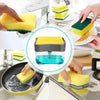 A hand is using a yellow sponge holder to dispense soap into a dish, demonstrating a 2-in-1 soap dispenser.