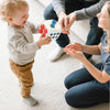 A toddler is playing with a white sensory ball featuring red and blue balls while being watched by an adult.