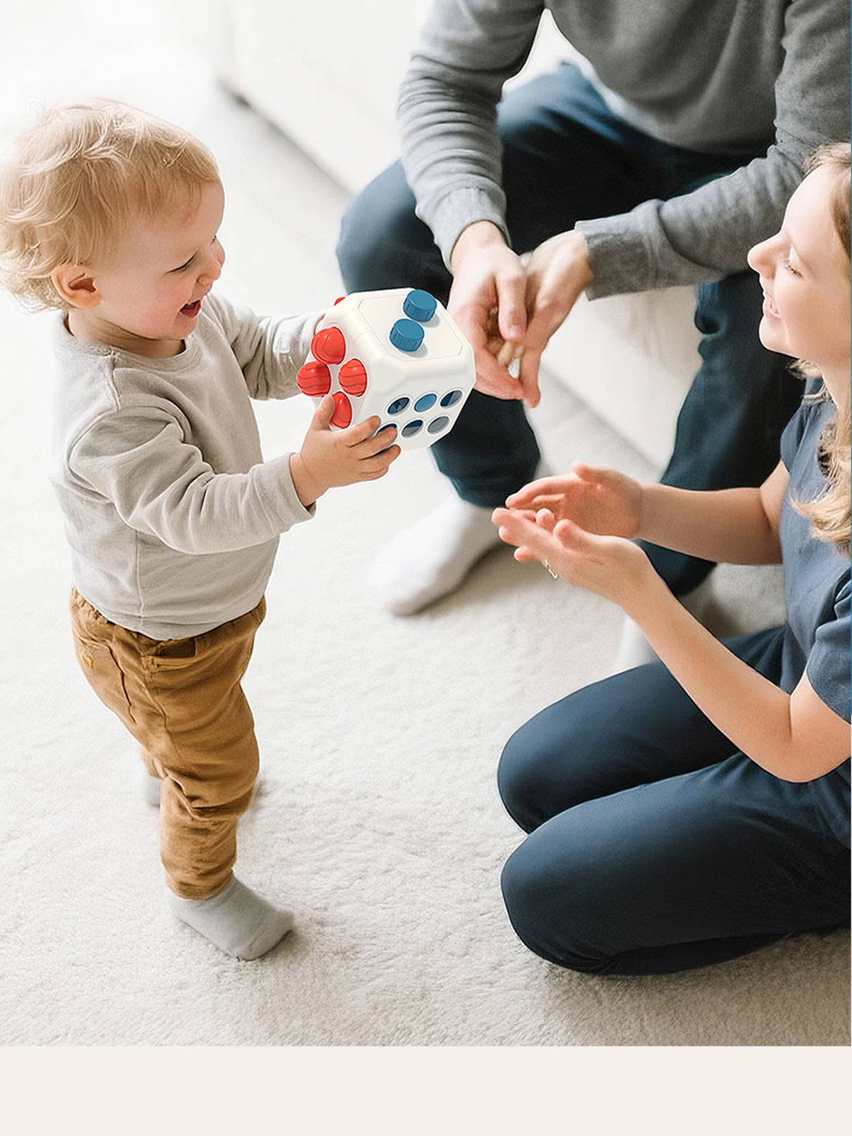 A toddler is playing with a white sensory ball featuring red and blue balls while being watched by an adult.
