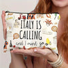 A hand holds an Italian souvenir travel makeup bag with a zipper, featuring text and illustrations.