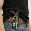 A black pistol-shaped keychain set with a key attached is clipped onto a brown leather belt and denim jeans.