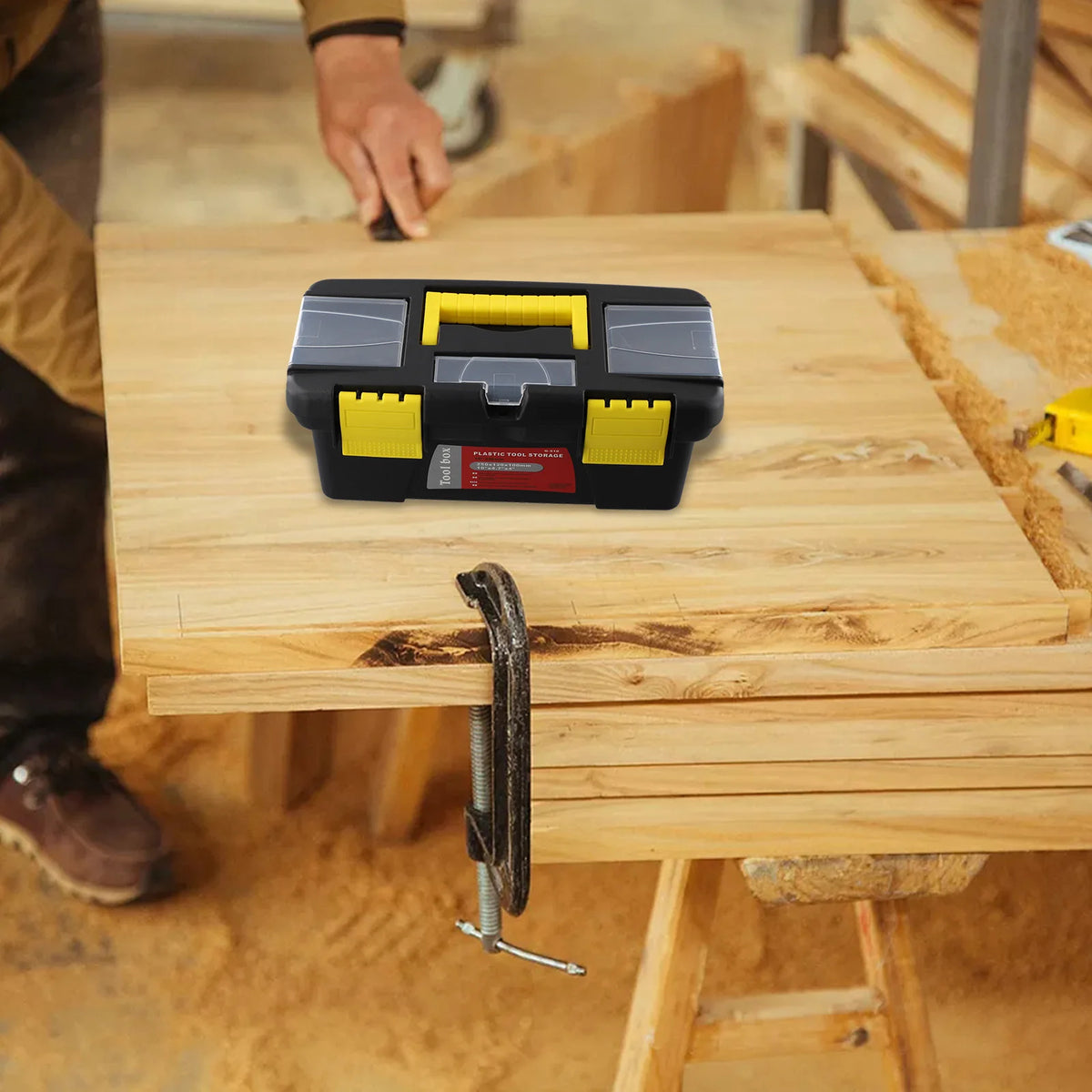 A black and yellow plastic toolbox is placed on a wooden workbench with a hand nearby.