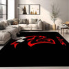 A black doormat with a red stylized logo is placed on a floor in a modern living room setting.