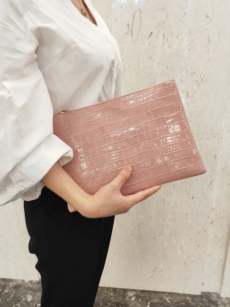 A woman holds a pink crocodile-embossed PU leather envelope clutch against a light background.