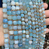 A close-up of various square faceted natural stone beads in shades of blue and white stacked on a hand.