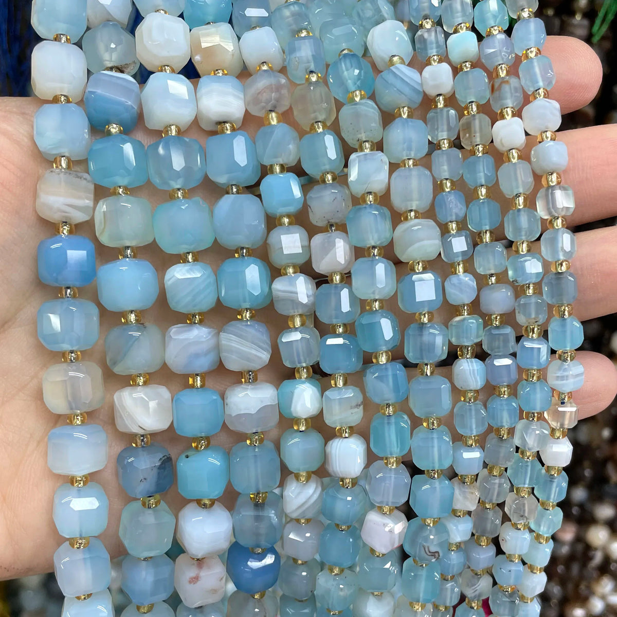 A close-up of various square faceted natural stone beads in shades of blue and white stacked on a hand.
