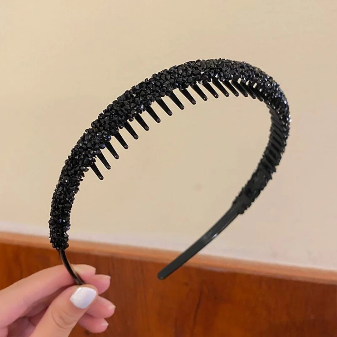 Primer plano de una diadema elástica con pedrería negra, sostenida por una mano.