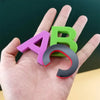A hand holds a magnetic alphabet learning set with the letters A and B in purple and green.