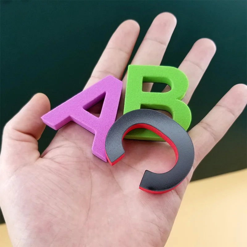 A hand holds a magnetic alphabet learning set with the letters A and B in purple and green.