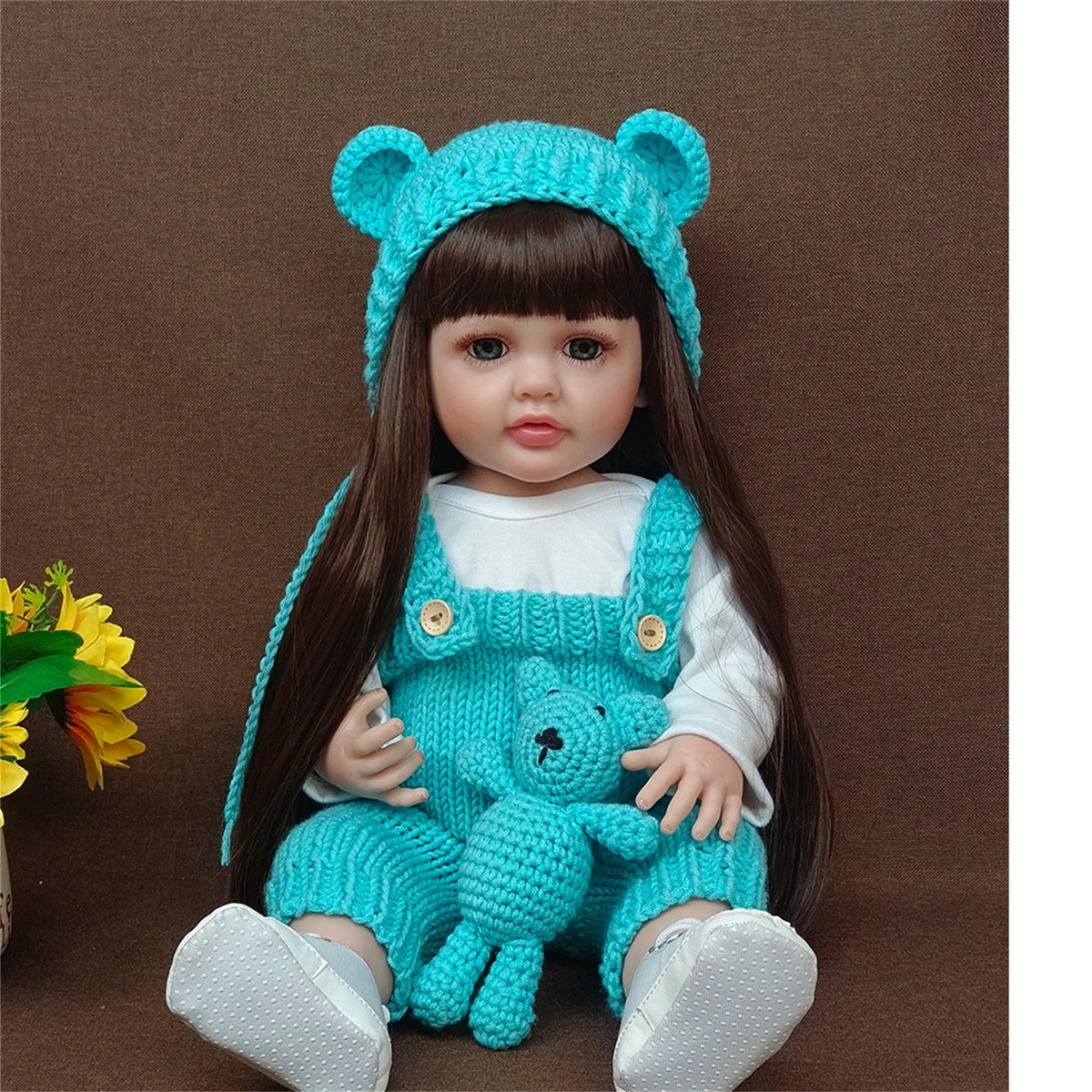 A lifelike silicone baby doll wearing a blue bear hat and matching outfit.