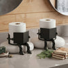 A black human-shaped freestanding toilet paper holder with white rolls sits on a light gray countertop.