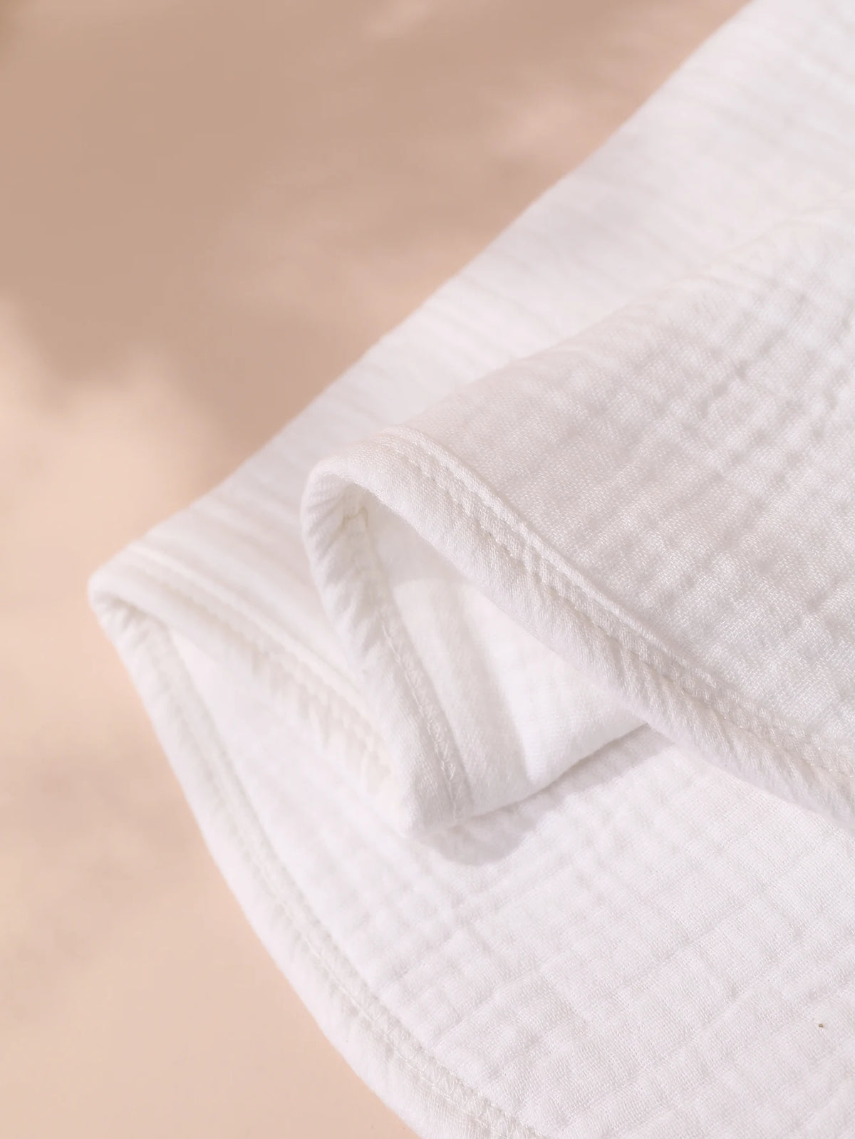 A white, folded baby burp cloth is shown in soft natural light.