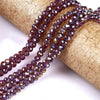 A strand of faceted purple crystal glass spacer beads is unwrapped on a gold-colored fabric roll.
