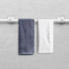 Two towels, one dark gray and one white, are hanging on a white curtain rod with adhesive clips.