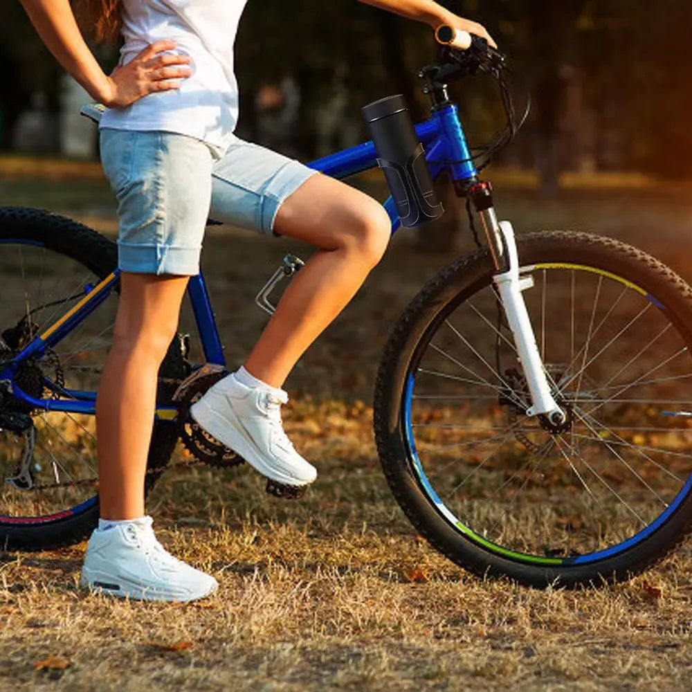A person is riding a blue bicycle with a bottle holder mounted on the handlebars in an outdoor setting.
