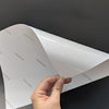 A hand is holding a sheet of glossy self-adhesive inkjet photo paper, showing the white surface and printed text.