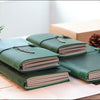 A stack of green handcrafted genuine leather refillable journals resting on a light surface.