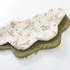 A light cream cotton baby feeding bib with a floral pattern and a darker olive green absorbent towel stacked together.