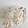 A rolled floral muslin baby blanket in cream and green tones.