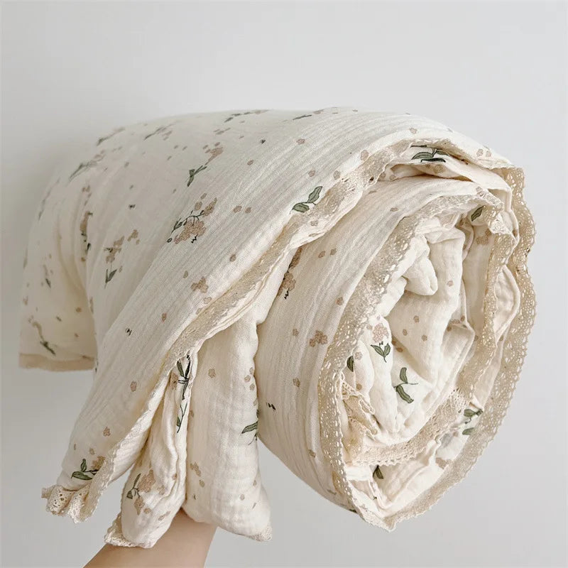 A rolled floral muslin baby blanket in cream and green tones.