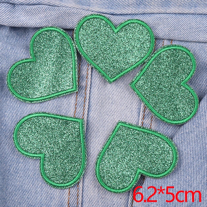 A set of five green glitter heart iron-on embroidered patches on a gray denim fabric.