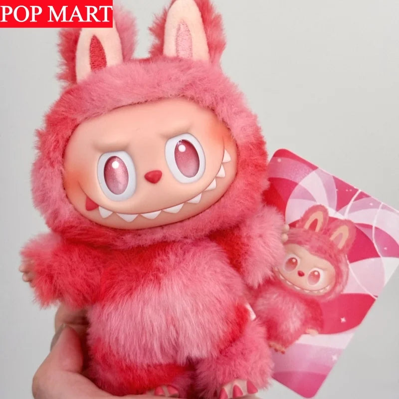 A pink fluffy Labubu plush doll with large eyes and white teeth is held in a hand.