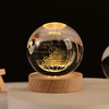 A spherical crystal ball night light with a golden internal glow resting on a natural wooden base.