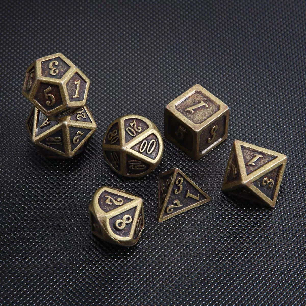 A collection of bronze metal polyhedral dice including a d6, d8, d10, d12, and d20 resting on a dark surface.
